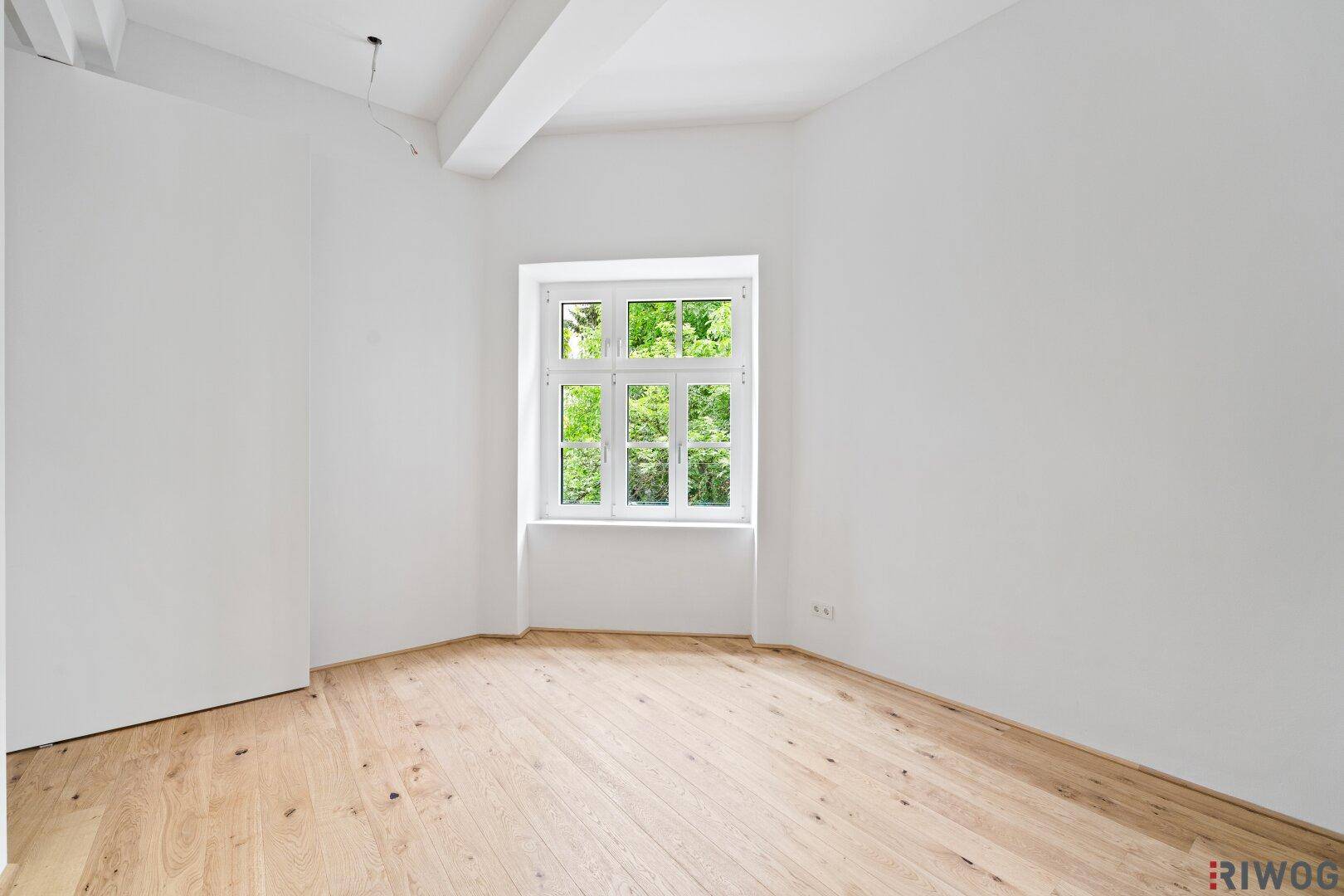 Ruhiges Zimmer mit Holzboden und einem Fenster, das viel Tageslicht hereinlässt.