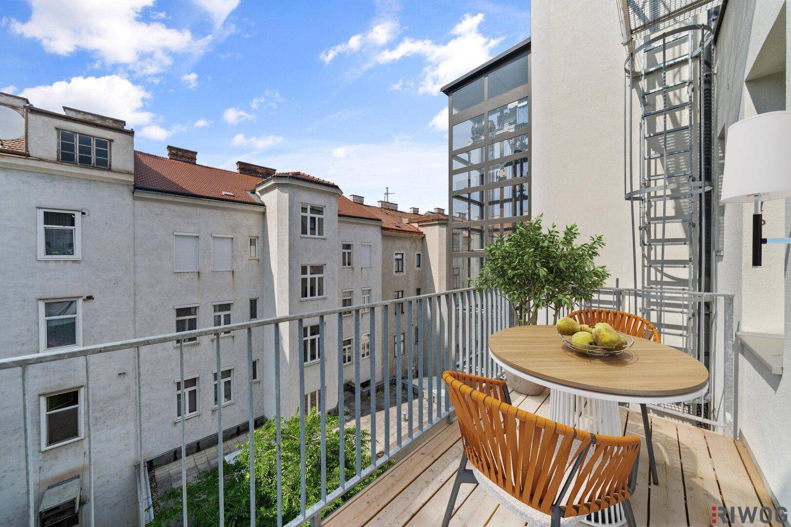 Heller Balkon mit Holzboden, modernen Sitzgelegenheiten und Blick auf die umliegenden Gebäude.