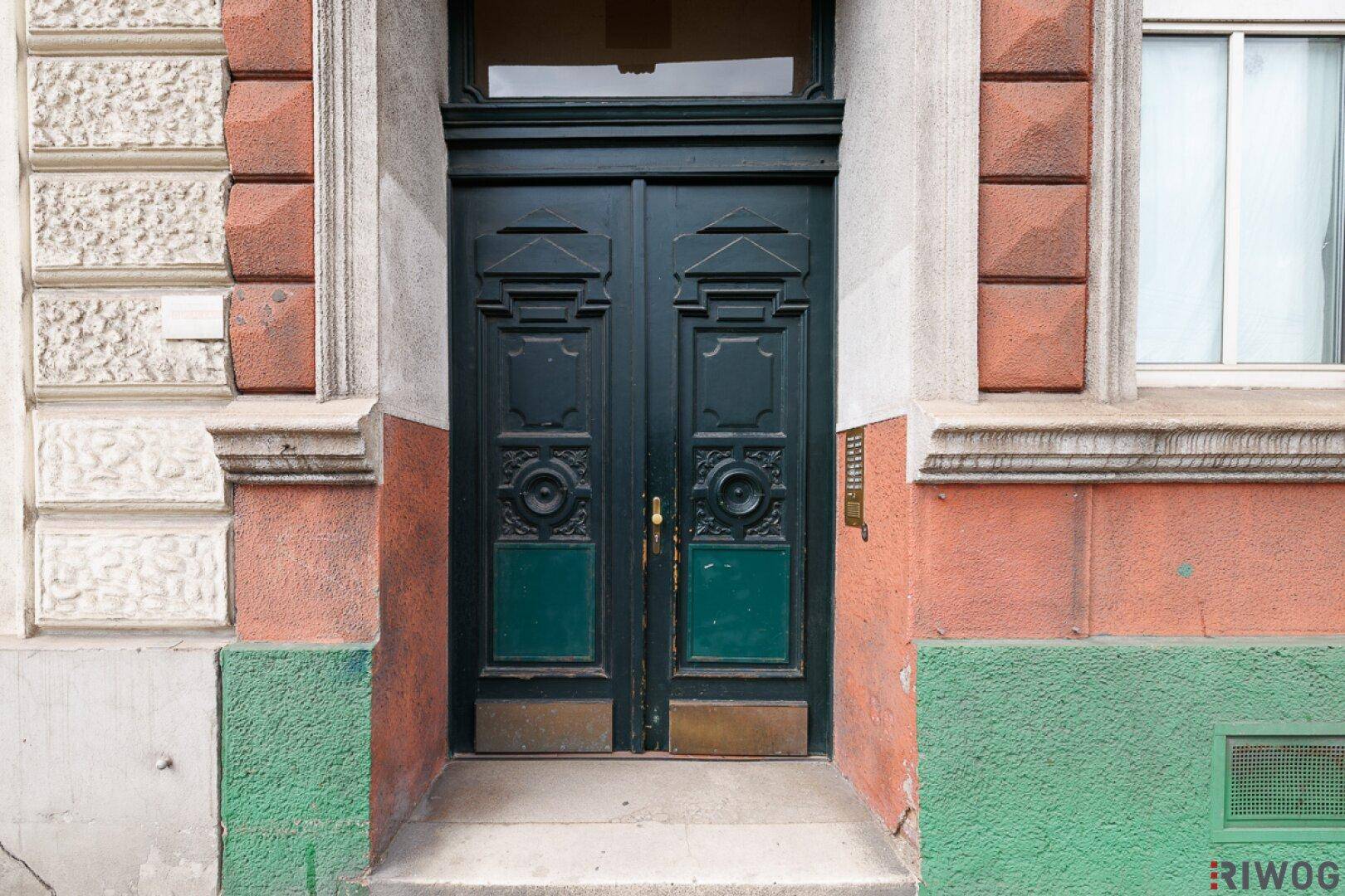 Prächtige, dunkelgrüne Eingangstür mit kunstvollen Schnitzereien in einer farbigen Fassade.