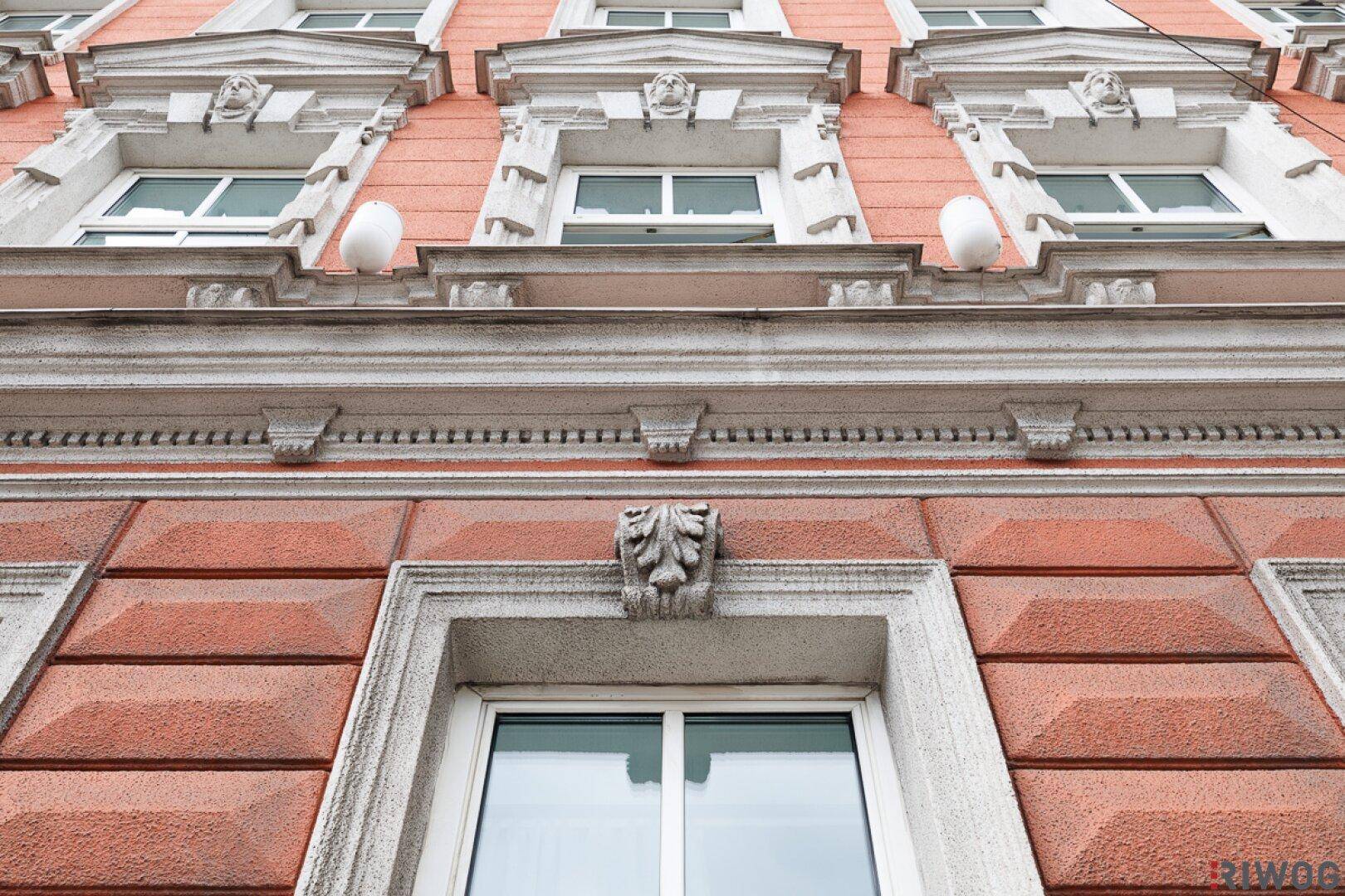 Detailaufnahme einer historischen Fassade mit kunstvollen Verzierungen und modernen Fenstern.