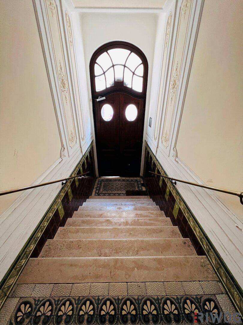 Elegantes Treppenhaus mit verzierten Wänden, Marmorstufen und einer kunstvollen Holztür am oberen Ende.