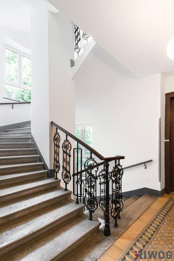 Historisches Treppenhaus mit schmiedeeisernem Geländer und hohen Wänden, die viel Licht hereinlassen.