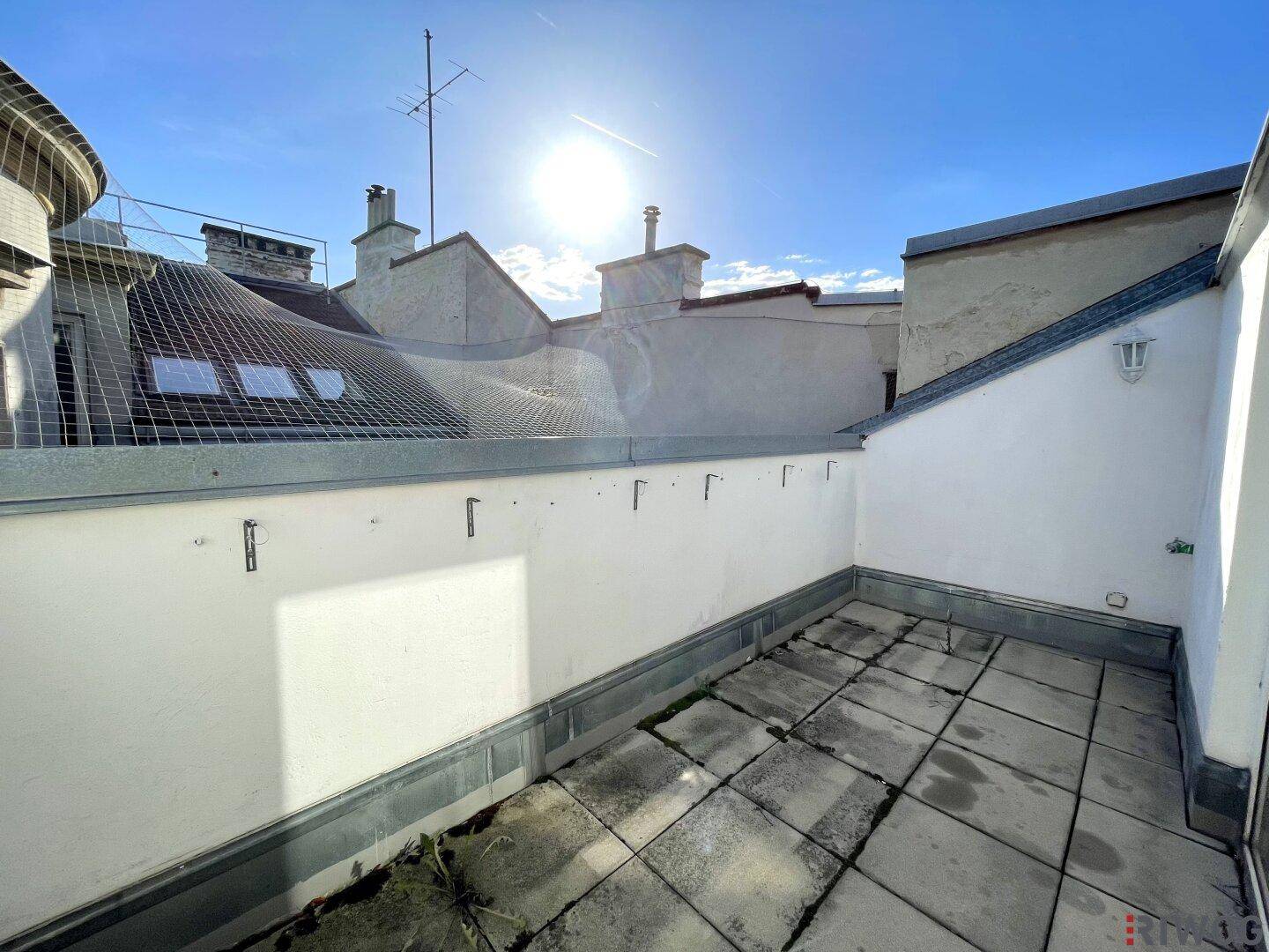 Sonniger Außenbereich mit Fliesenboden und Blick auf die umliegenden Dächer der Stadt.