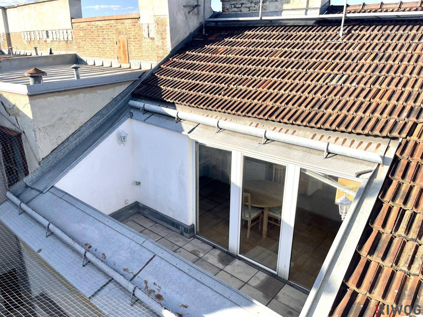 Dachterrasse mit Zugang zum Innenbereich und Blick auf die umliegenden Dächer der Stadt.