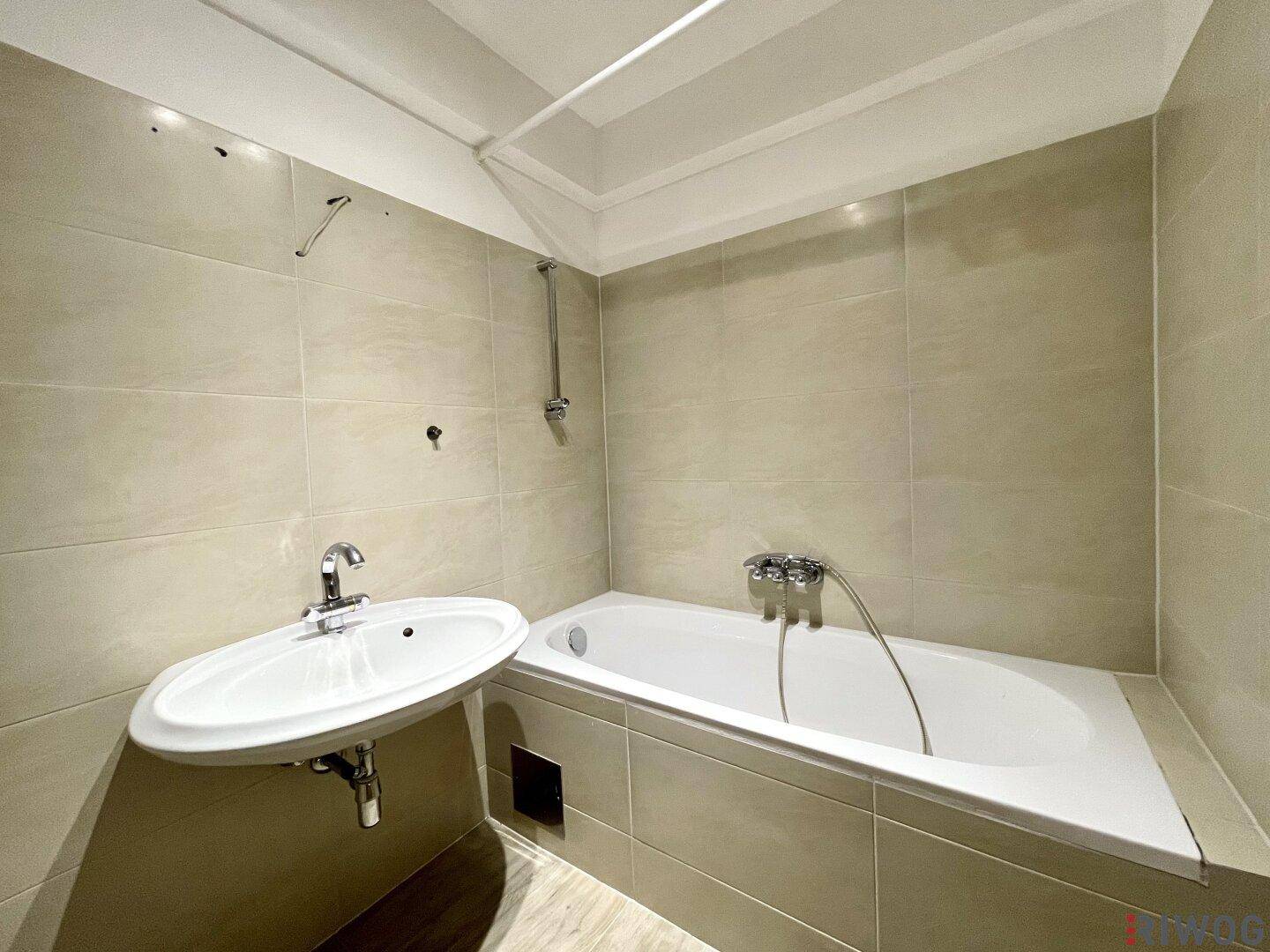 Funktionales Badezimmer mit Badewanne, Waschbecken und hellen Fliesen an Wänden und Boden.