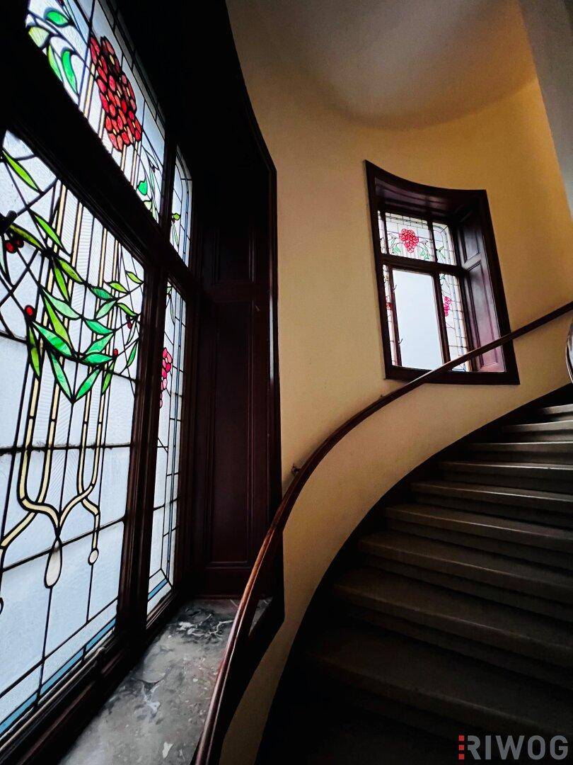 Historisches Treppenhaus mit kunstvollen Buntglasfenstern, die für eine besondere Atmosphäre sorgen.