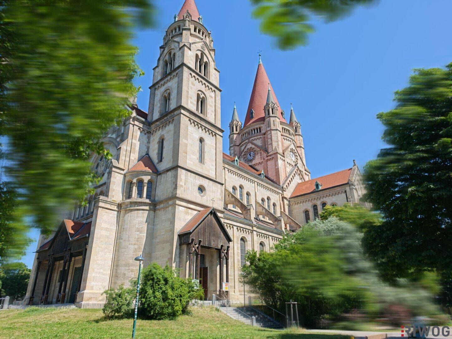 Historische Kirche mit markanten Türmen und rotem Dach, umgeben von üppigem Grün.