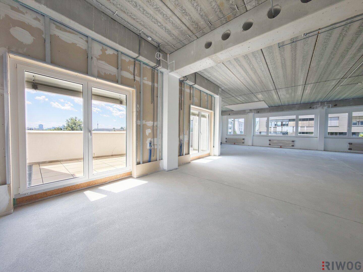 Unfertiger Büroraum mit Betonwänden und -decke, bereit für den Innenausbau und mit Balkonzugang.