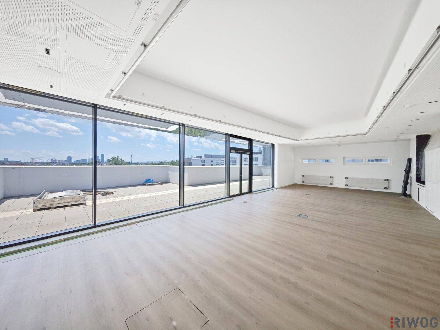 Geräumiger, leerer Büroraum mit großen Fenstern und Zugang zu einer Außenterrasse, bereit für den Ausbau.