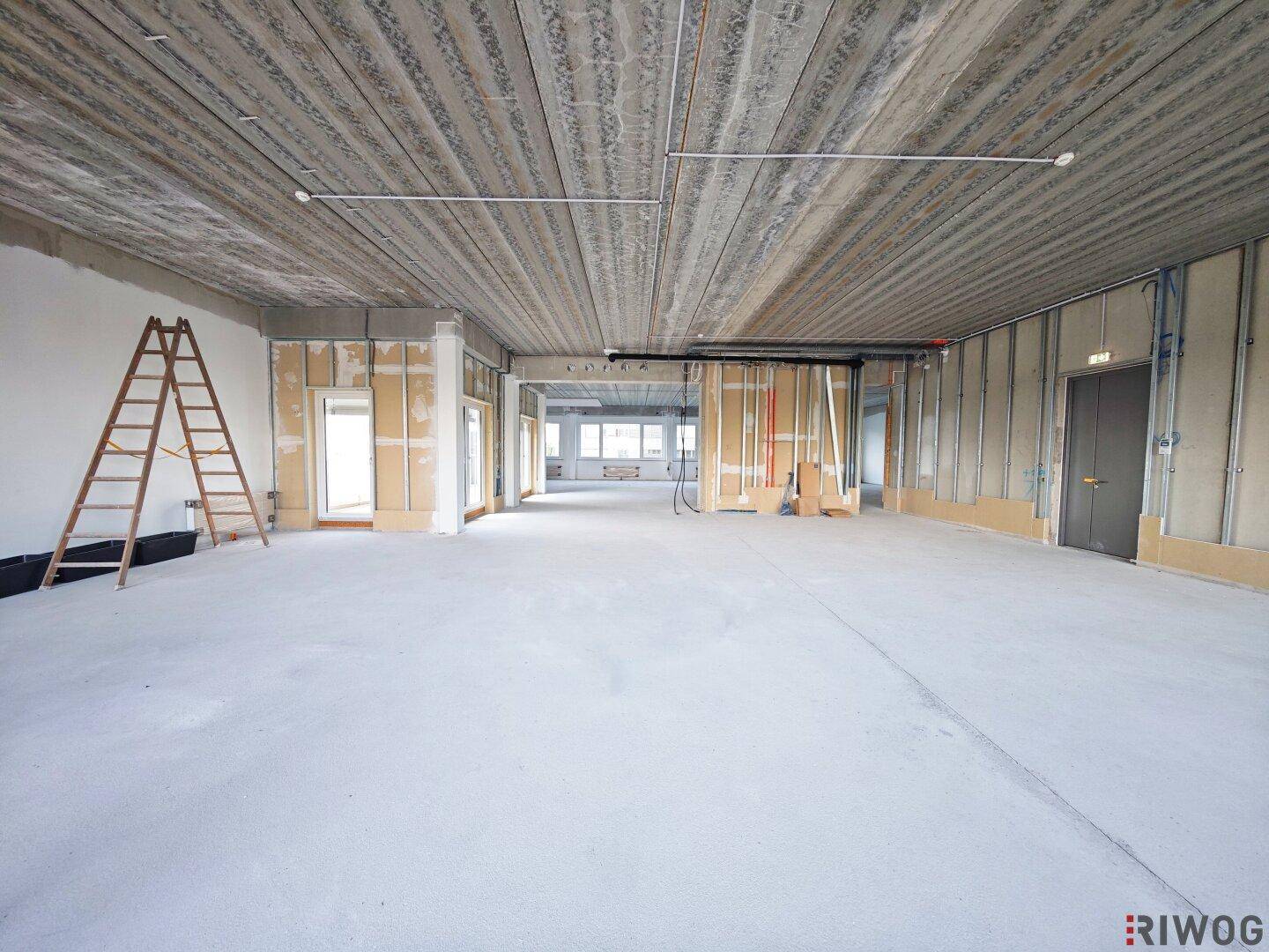 Großer, offener Bürobereich im Rohbau mit sichtbarer Betondecke und vorbereiteten Wänden für den Ausbau.