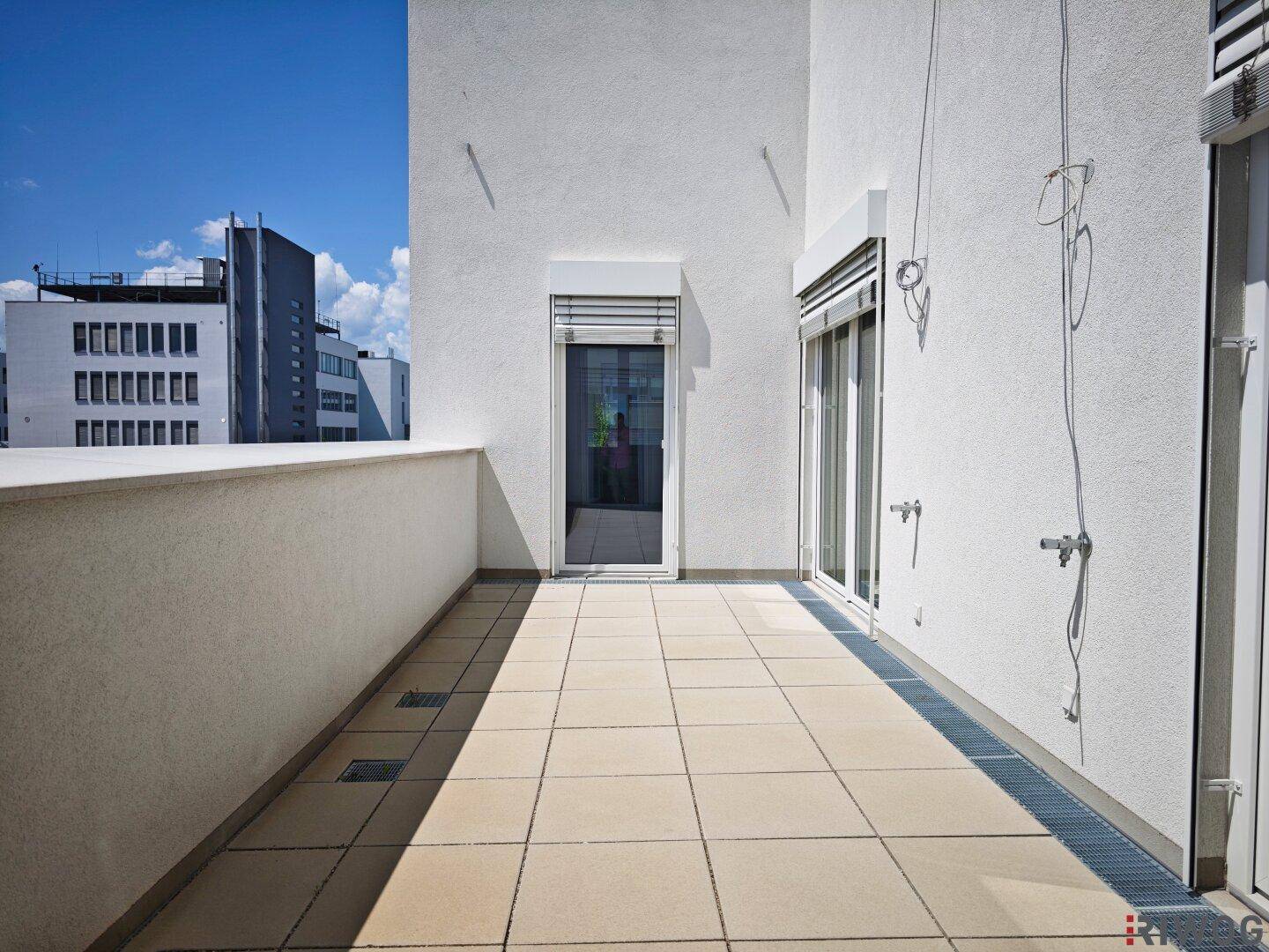 Heller Balkon mit beigefarbenen Fliesen und weißen Wänden, ausgestattet mit Rollläden für Privatsphäre.