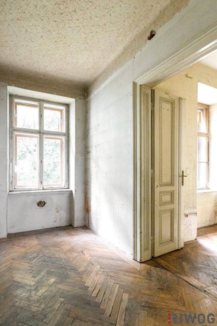 Leerer Raum mit abgenutztem Fischgrätparkett und einem Fenster, das Tageslicht spendet.