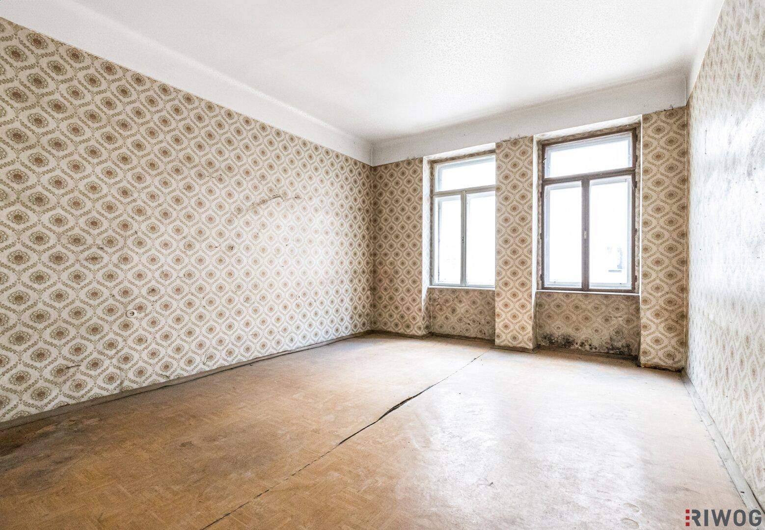 Leerer Raum mit alter Tapete und renovierungsbedürftigem Holzboden, bereit zur Sanierung.