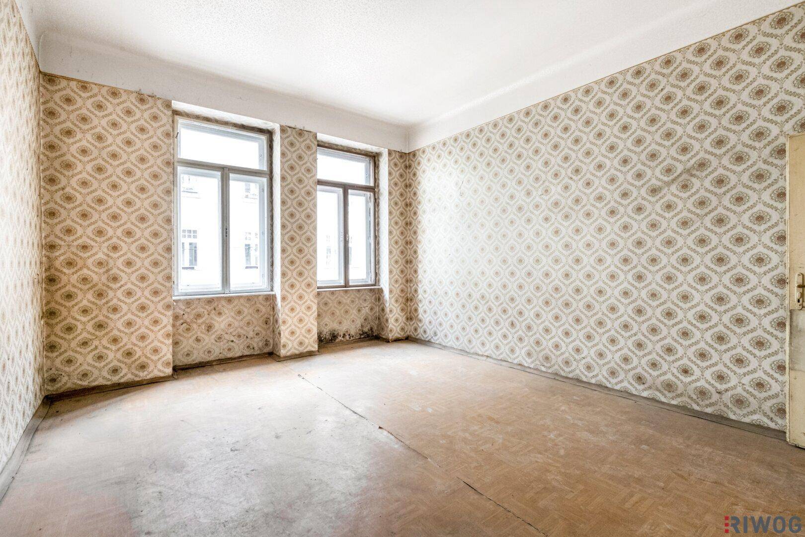 Leerer Raum mit alter Tapete und renovierungsbedürftigem Holzboden, bereit zur Sanierung.