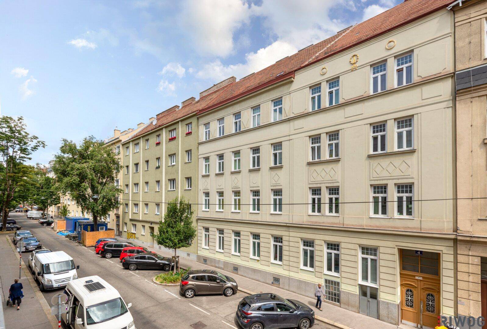 Blick auf die Straße mit parkenden Autos und der Fassade eines historischen Mehrfamilienhauses.