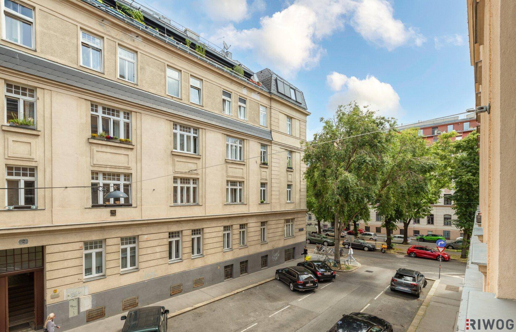 Ansicht der Gebäudefassade und der belebten Straße mit Bäumen und parkenden Fahrzeugen.