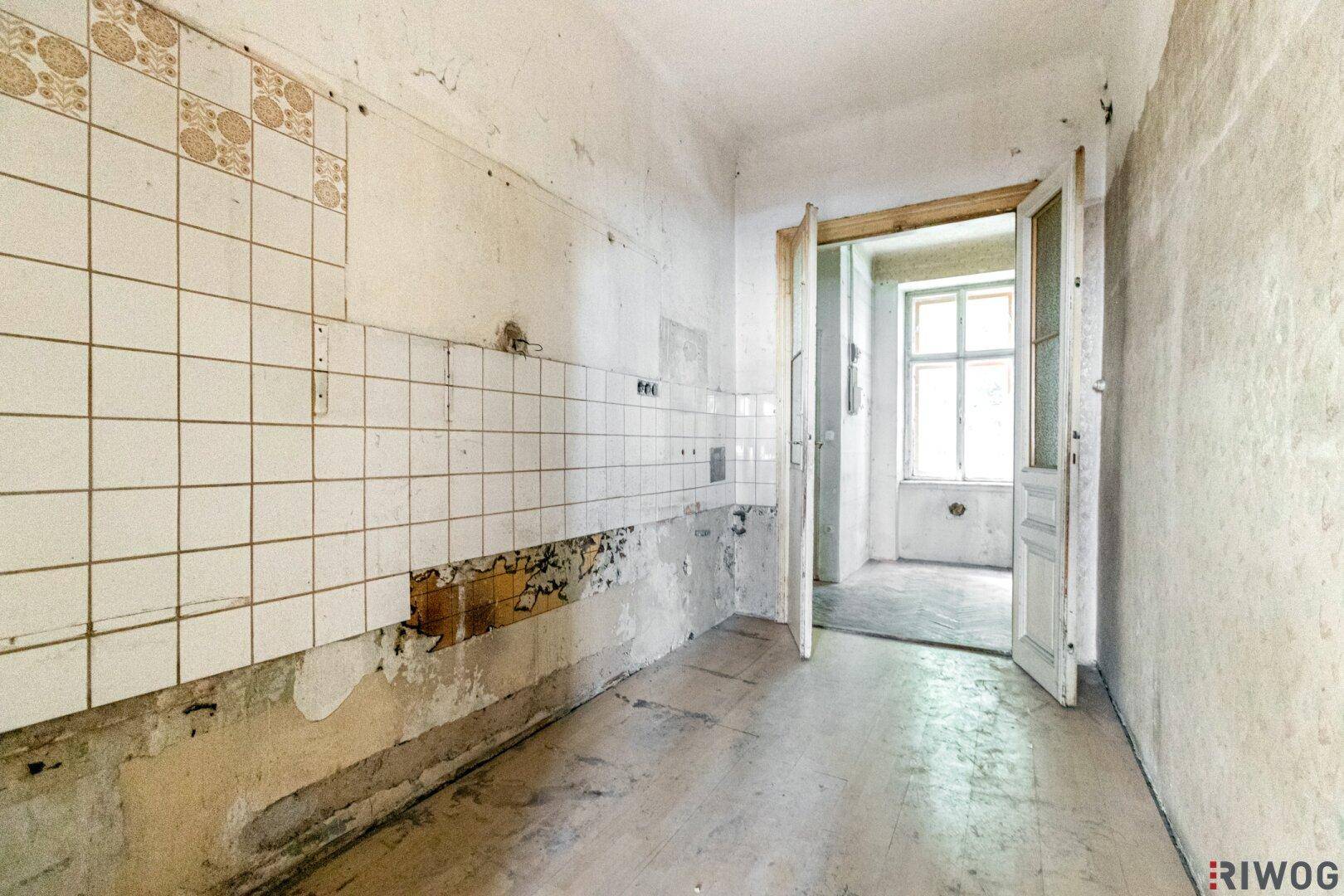 Renovierungsbedürftige Küche mit alten Fliesen und abgenutzten Wänden, bereit zur Sanierung.