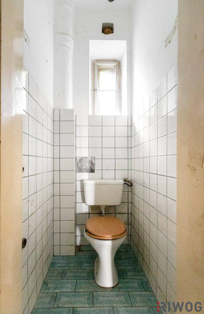 Kleines WC mit weißen Wandfliesen und einem Fenster, das Tageslicht hereinlässt.