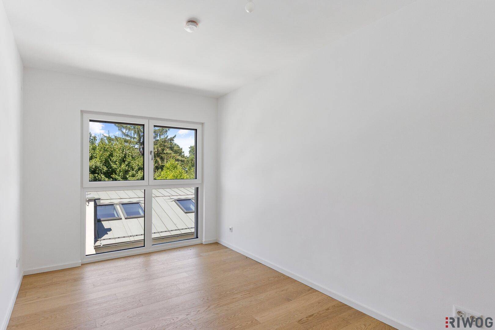 Helles Schlafzimmer mit Parkettboden und großem Fenster mit Blick auf die Umgebung.