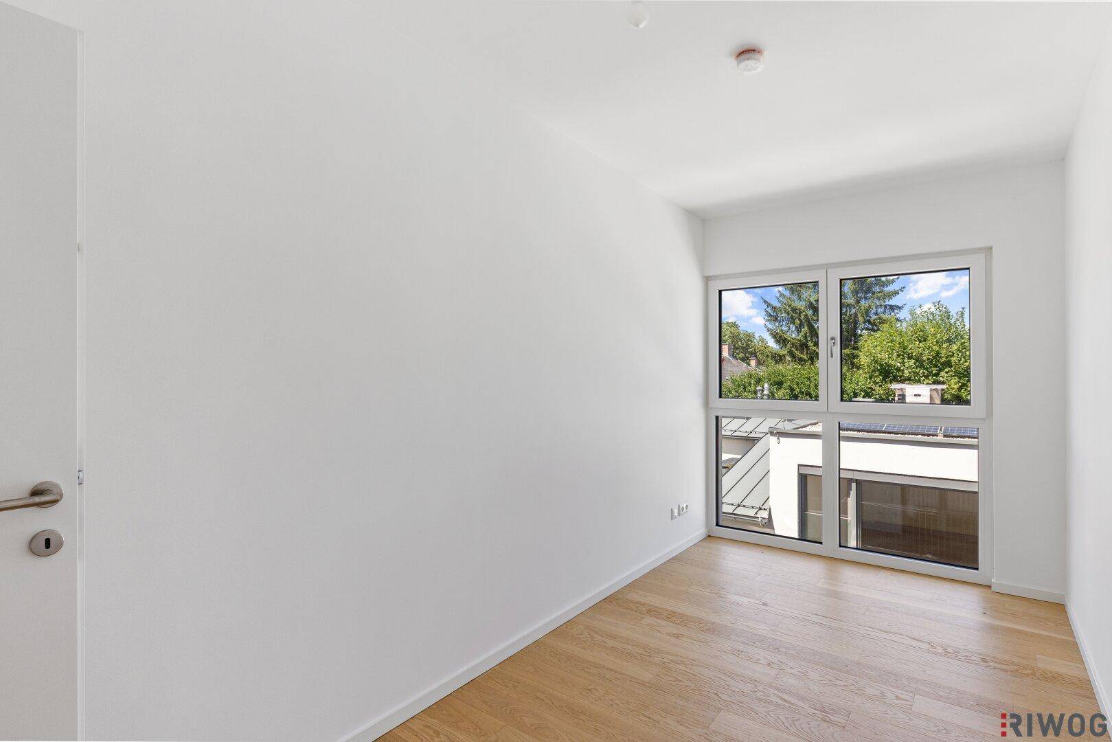 Freundliches Schlafzimmer mit viel Tageslicht und Blick ins Grüne durch das große Fenster.