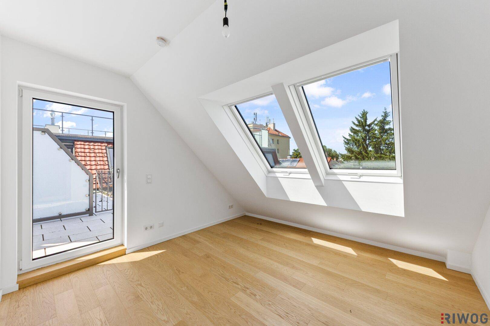 Dachgeschosszimmer mit Parkettboden, Dachschrägen und Zugang zu einer privaten Terrasse.