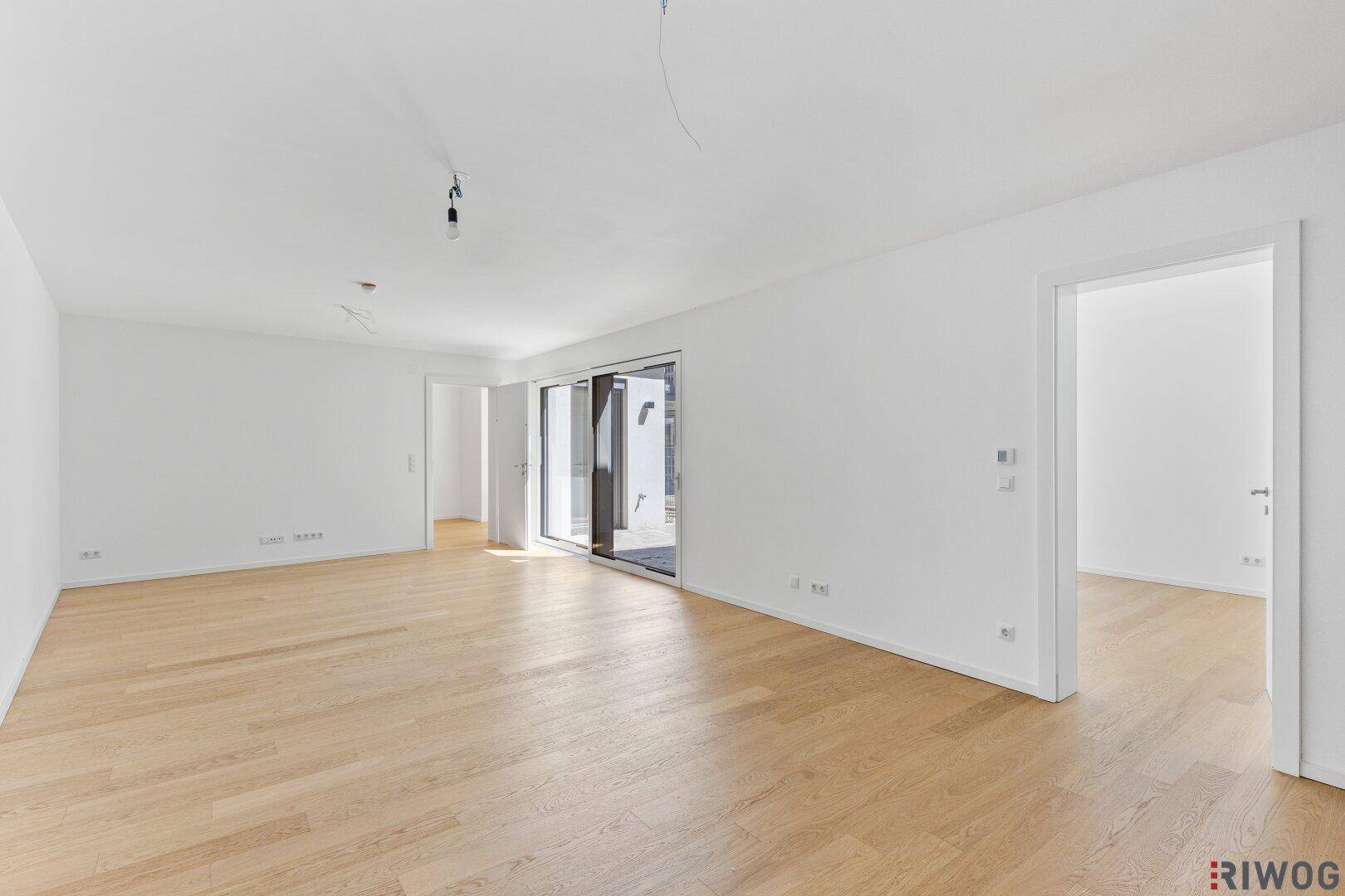 Geräumiges, unmöbliertes Wohnzimmer mit hellem Parkettboden und Zugang zu weiteren Räumen.