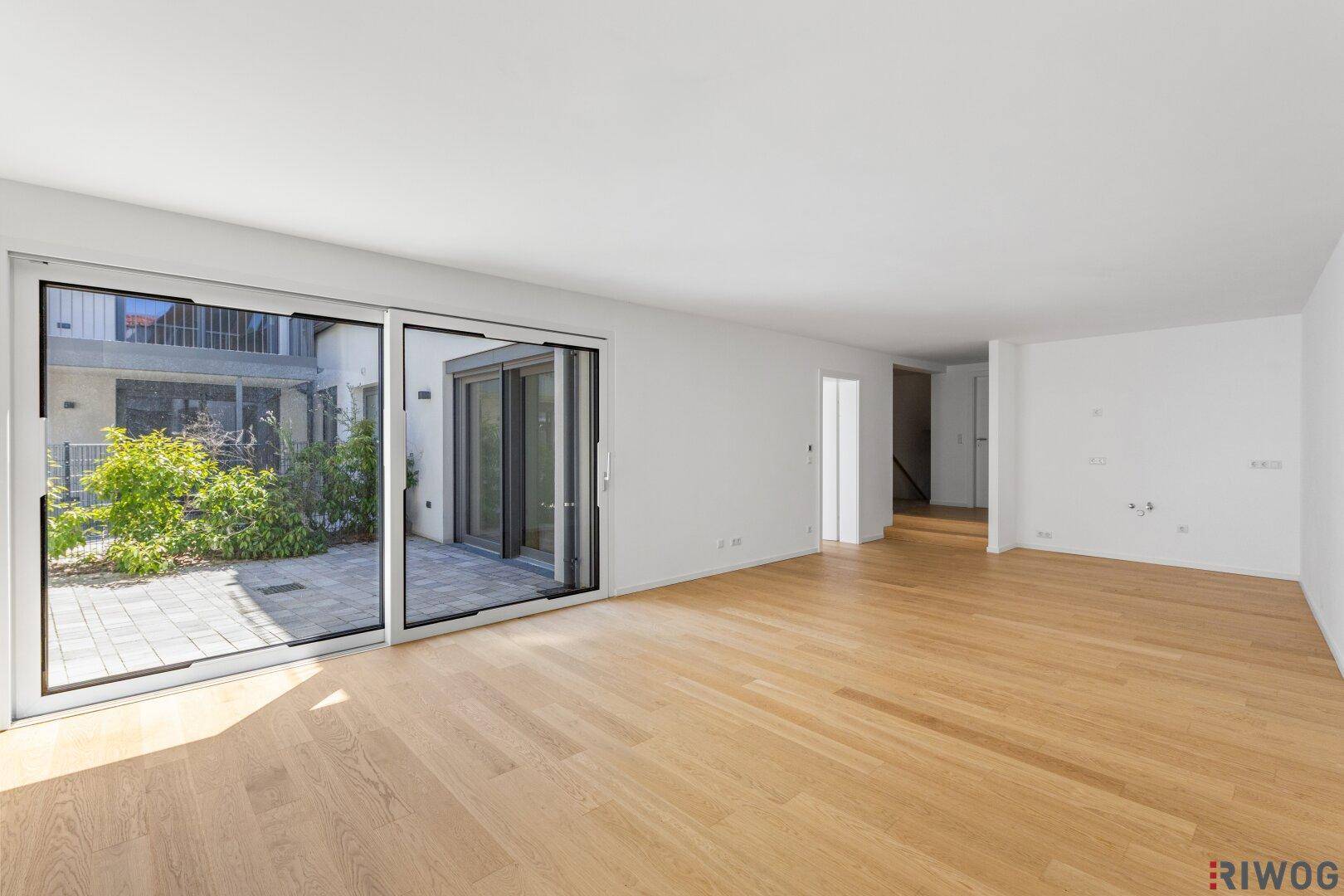 Helles, leeres Wohnzimmer mit großen Schiebetüren zur Terrasse und Holzparkettboden.