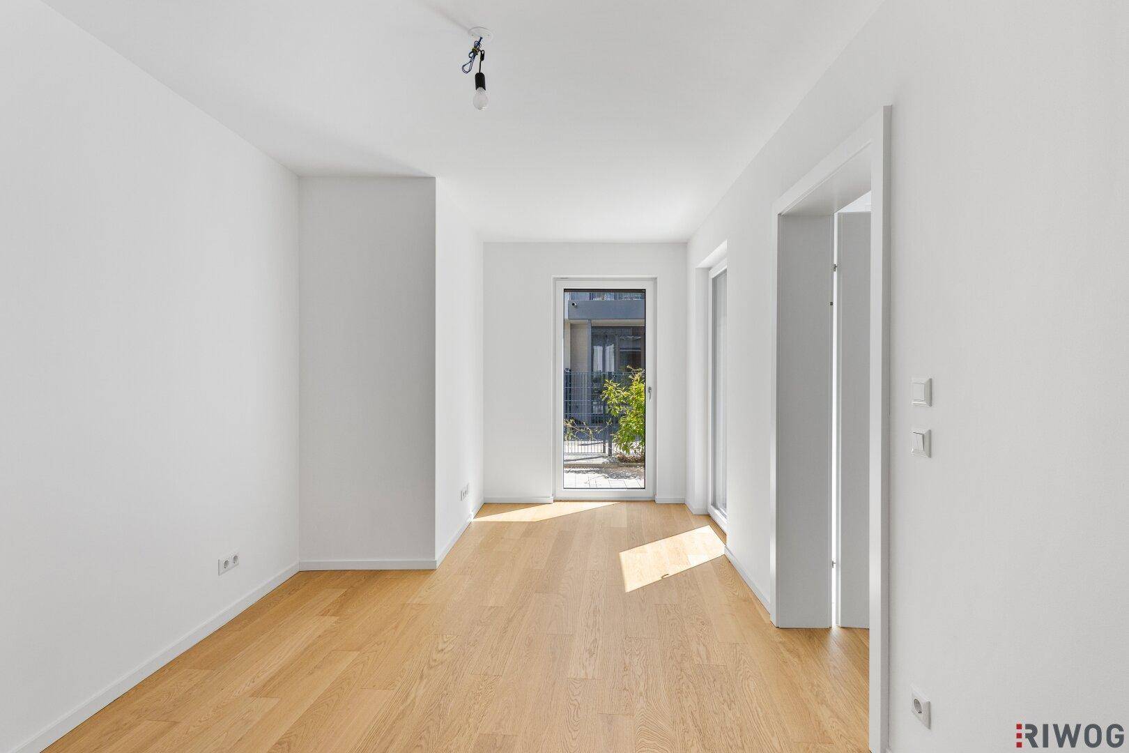 Lichtdurchfluteter Raum mit Holzboden und Fenstertür zum Außenbereich.