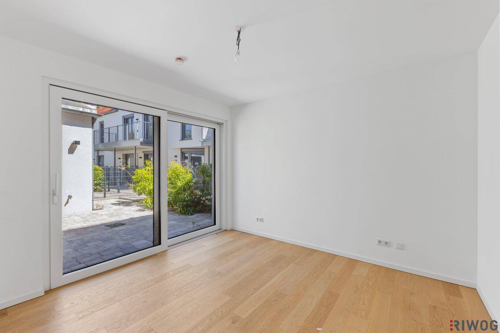 Helles Zimmer mit Schiebetür zum Außenbereich und modernem Holzparkettboden.