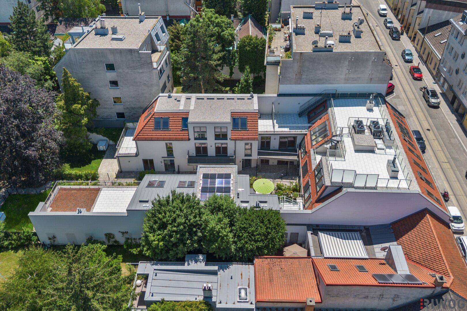 Luftaufnahme einer Wohnsiedlung mit verschiedenen Dächern und angrenzender Straße.