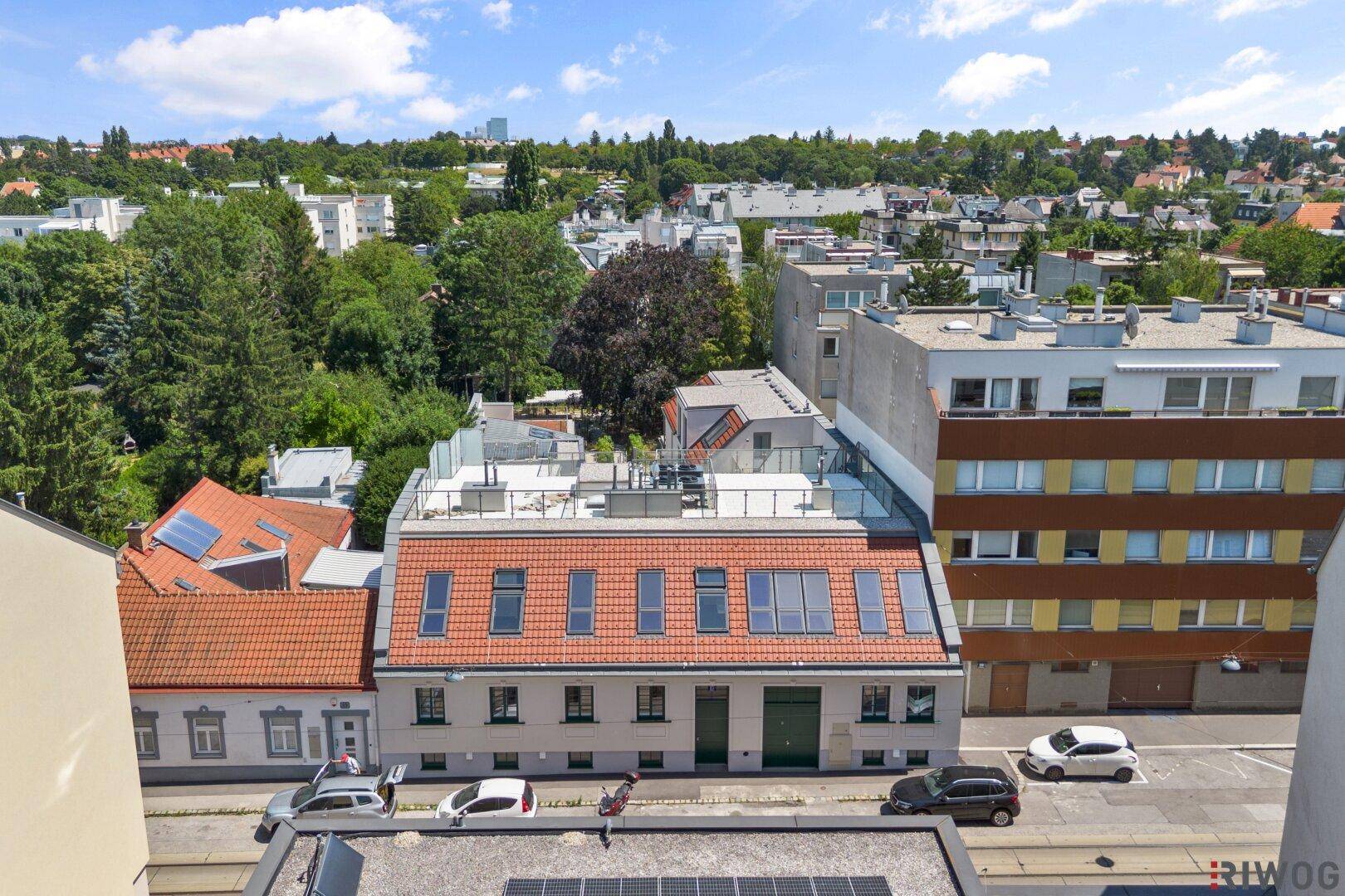 Blick über die Dächer der Stadt mit Wohngebäuden und grünen Hügeln im Hintergrund.