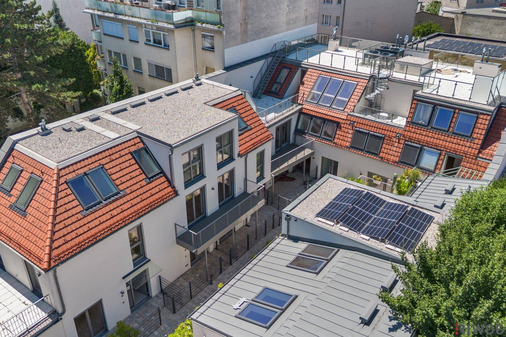 Luftaufnahme einer Wohnanlage mit verschiedenen Dächern, Balkonen und Solaranlagen.