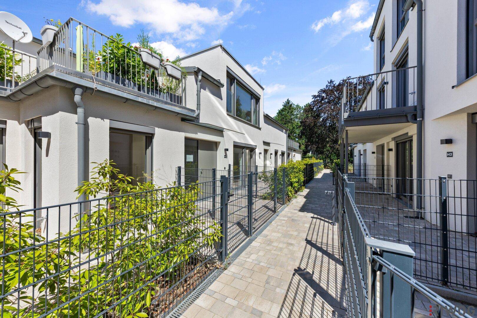 Gehweg zwischen modernen Wohngebäuden mit kleinen Gärten und Balkonen.