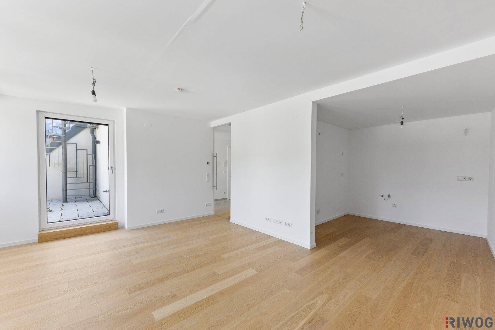Geräumiger, leerer Raum mit hellem Parkettboden und Zugang zu einem Balkon.