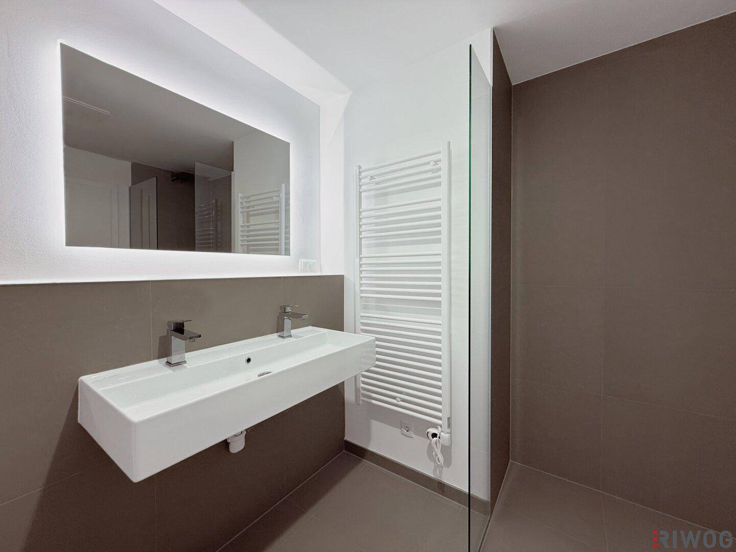 Stilvolles Badezimmer mit modernem Waschbecken, beleuchtetem Spiegel und praktischem Handtuchheizkörper.