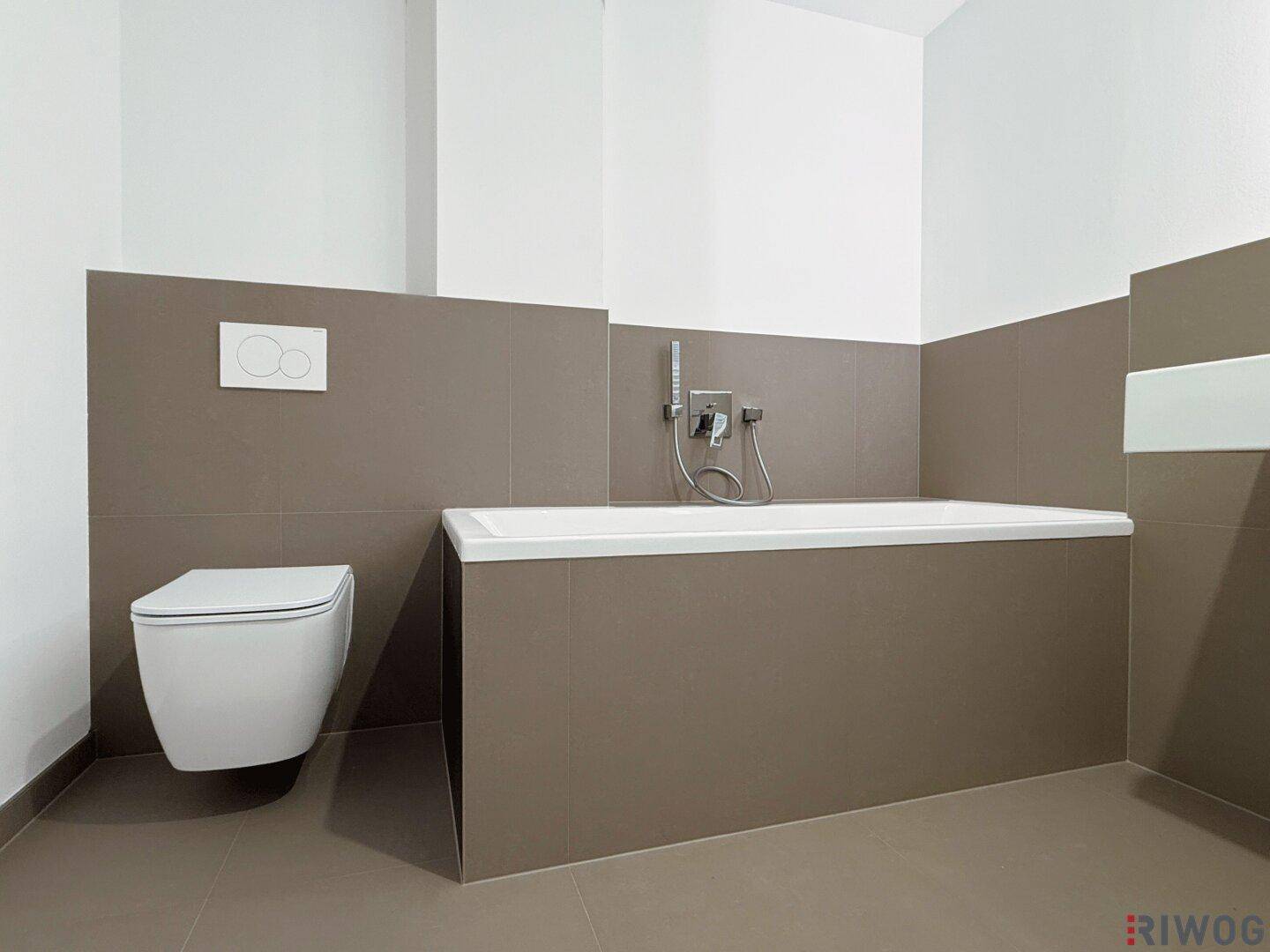 Zeitgemäßes Badezimmer mit integrierter Badewanne und wandhängendem WC, in neutralen Grautönen gehalten.