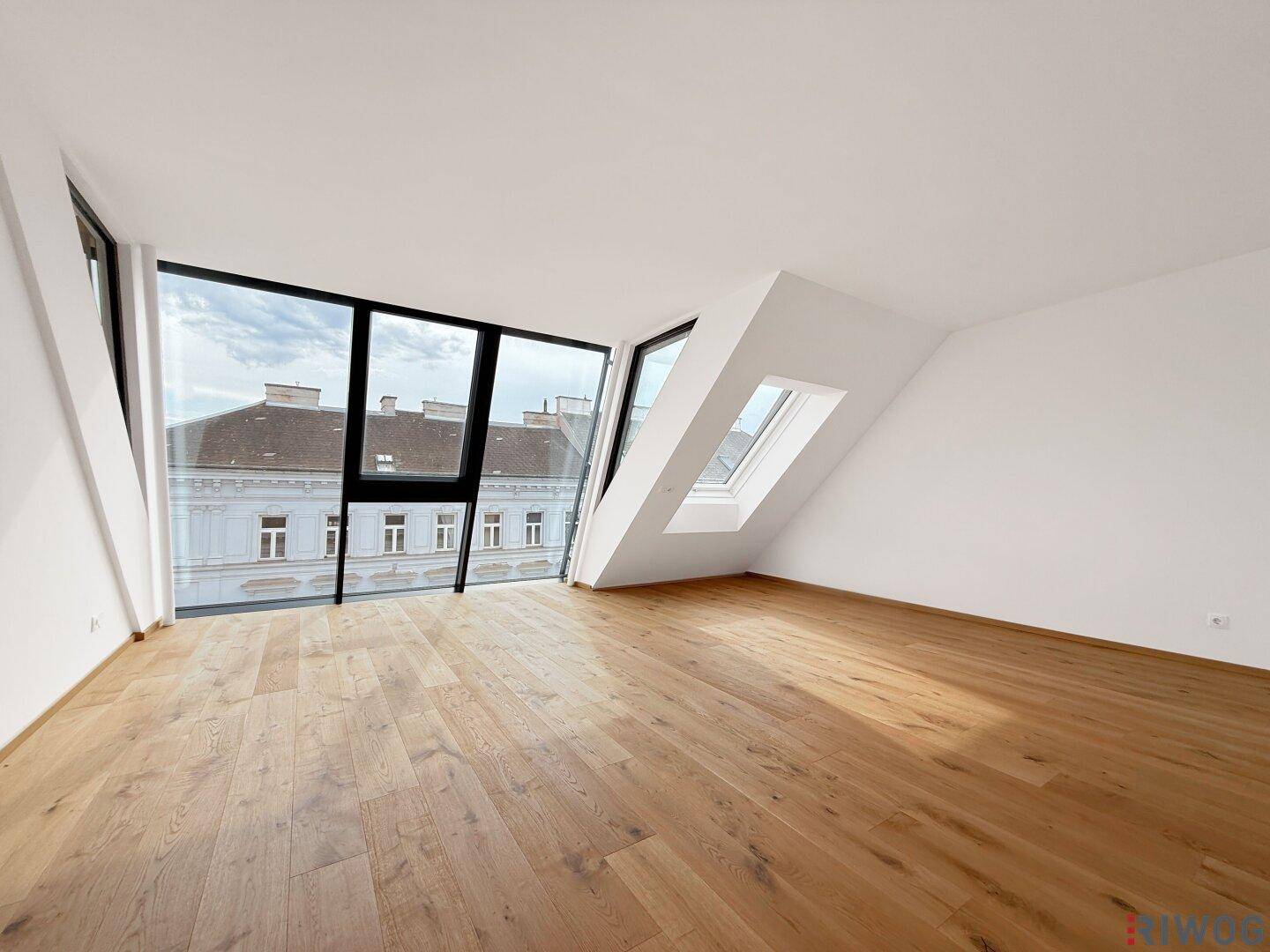 Helles Zimmer mit großen Fenstern, Dachschräge und Holzboden, bietet einen weiten Stadtblick.