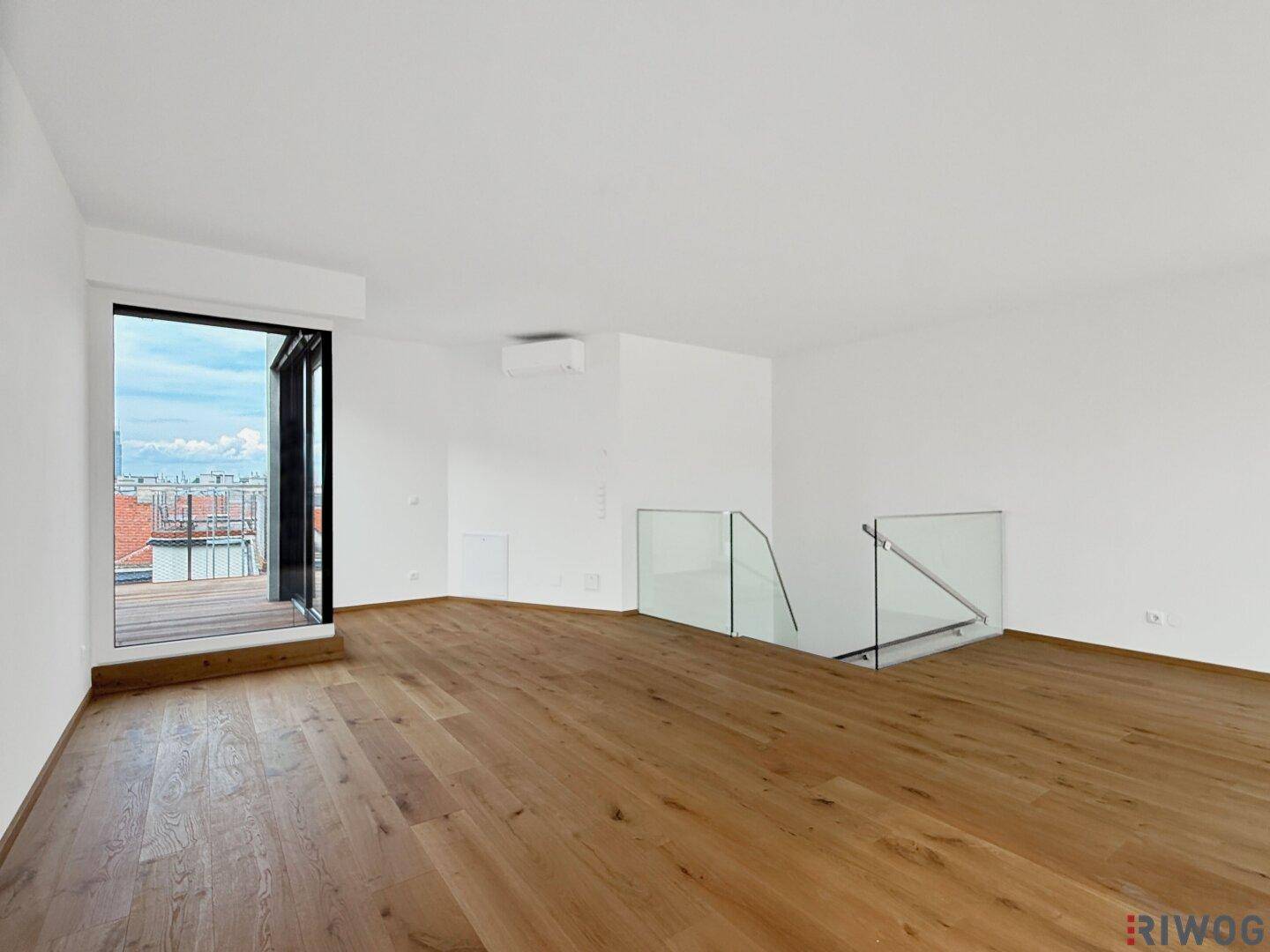 Geräumiger Wohnbereich mit Holzboden, Zugang zur Terrasse und moderner Glasbrüstung.