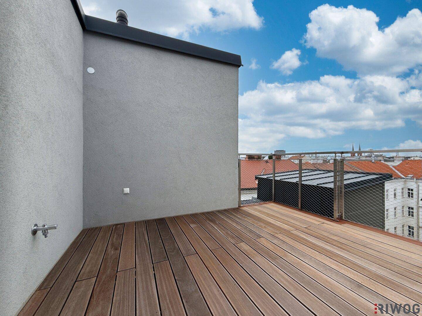 Moderne Dachterrasse mit Holzboden und Blick über die städtische Umgebung unter blauem Himmel.