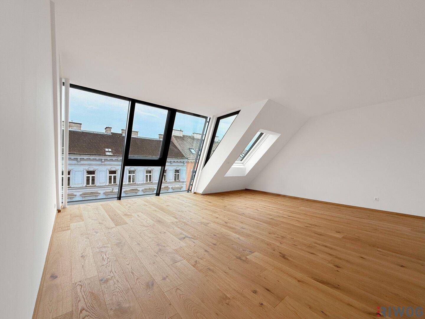 Lichtdurchfluteter Raum mit schrägen Wänden, großen Fenstern und Holzboden, ideal für modernes Wohnen.