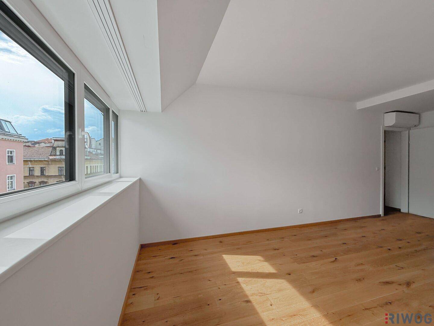 Helles Zimmer mit Holzboden, breitem Fenster und Dachschräge, bietet einen angenehmen Ausblick.