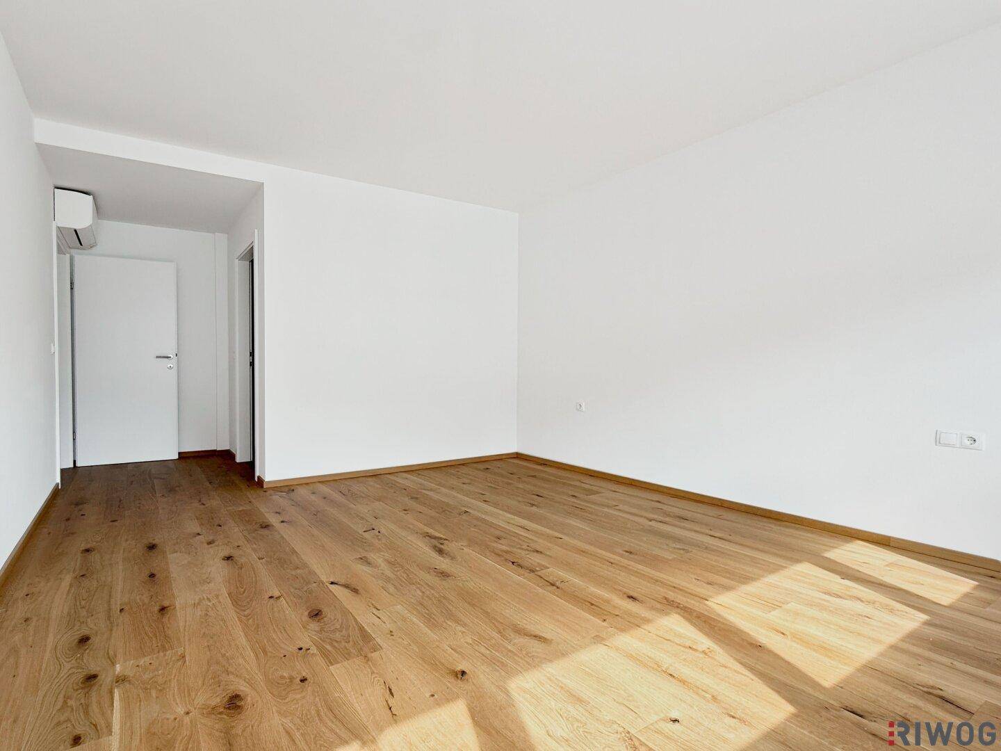 Geräumiges Zimmer mit Holzboden, weiß gestrichenen Wänden und Klimaanlage für angenehmes Raumklima.