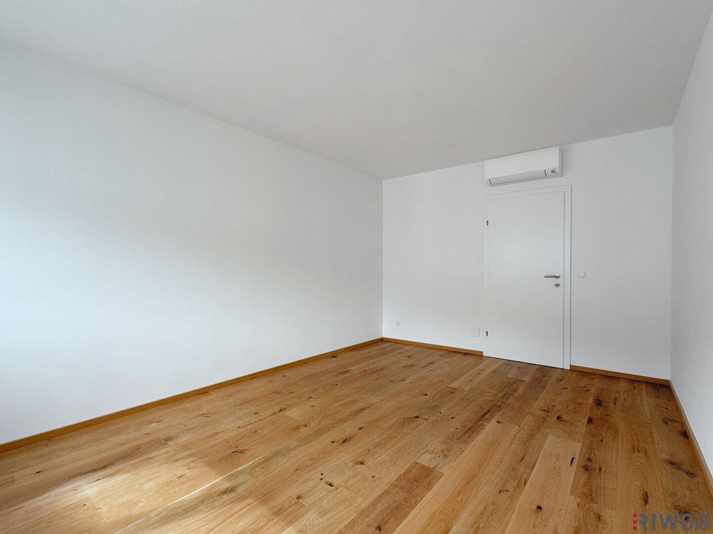 Helles Zimmer mit Holzboden, weiß gestrichenen Wänden und Klimaanlage, bereit zum Einrichten.