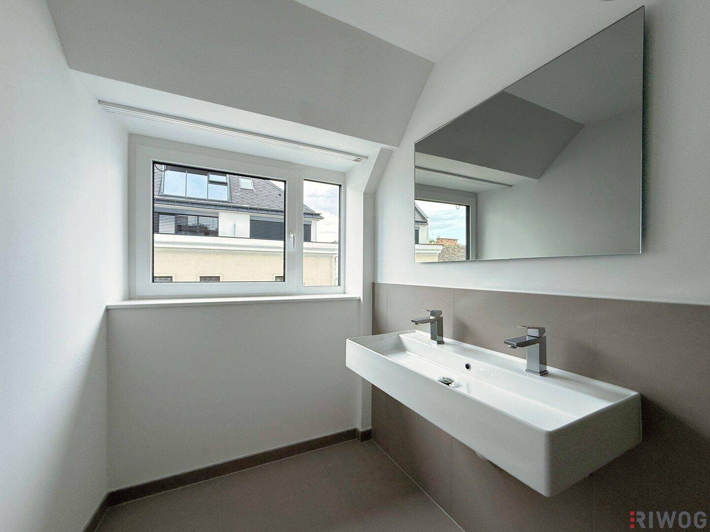 Modernes Badezimmer mit Doppelwaschbecken, großem Spiegel und Fenster, das für Helligkeit sorgt.