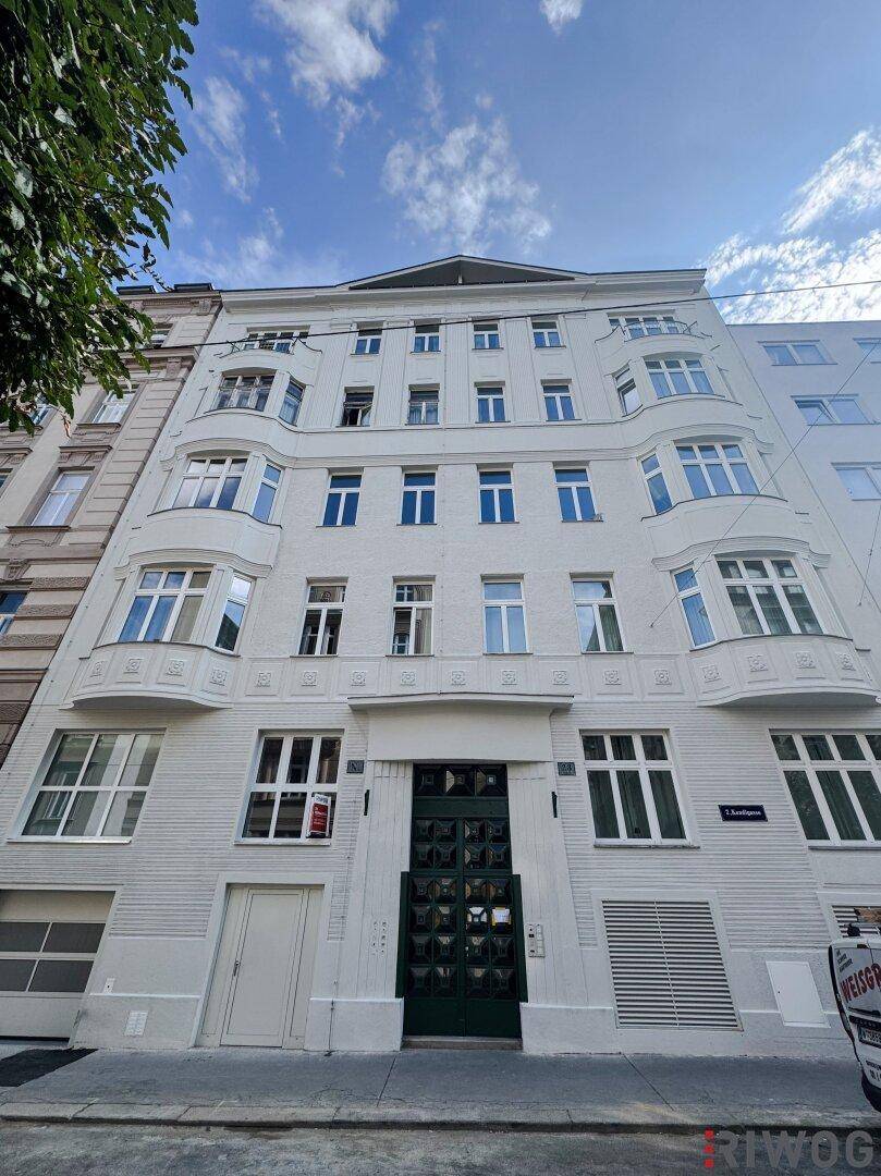 Weißes Mehrfamilienhaus mit klassischer Architektur, Erkerfenstern und einer markanten grünen Eingangstür unter blauem Himmel.