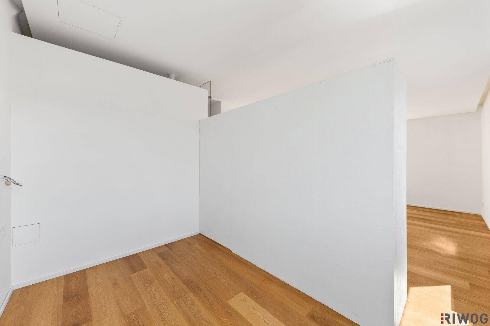 Heller, leerer Raum mit Holzboden und einer Trennwand, ideal als Schlafbereich.