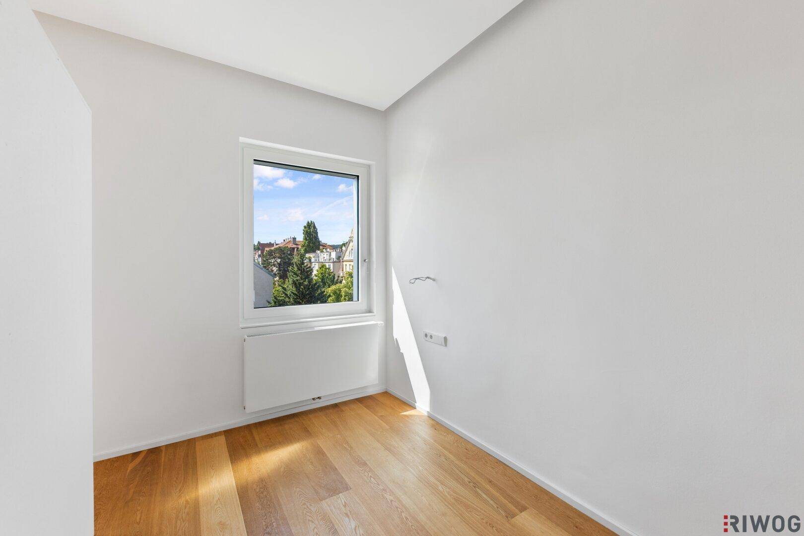 Leeres Zimmer mit Holzboden, weißen Wänden und Blick auf die Straße.