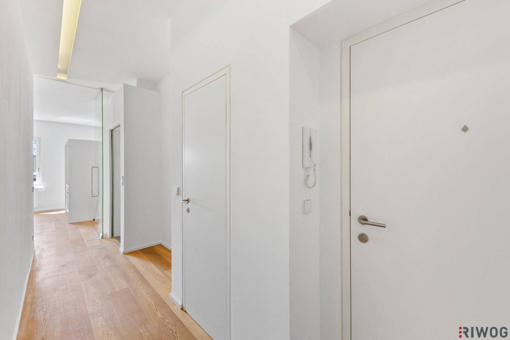 Heller Flur mit Holzboden, weißen Türen und Gegensprechanlage.