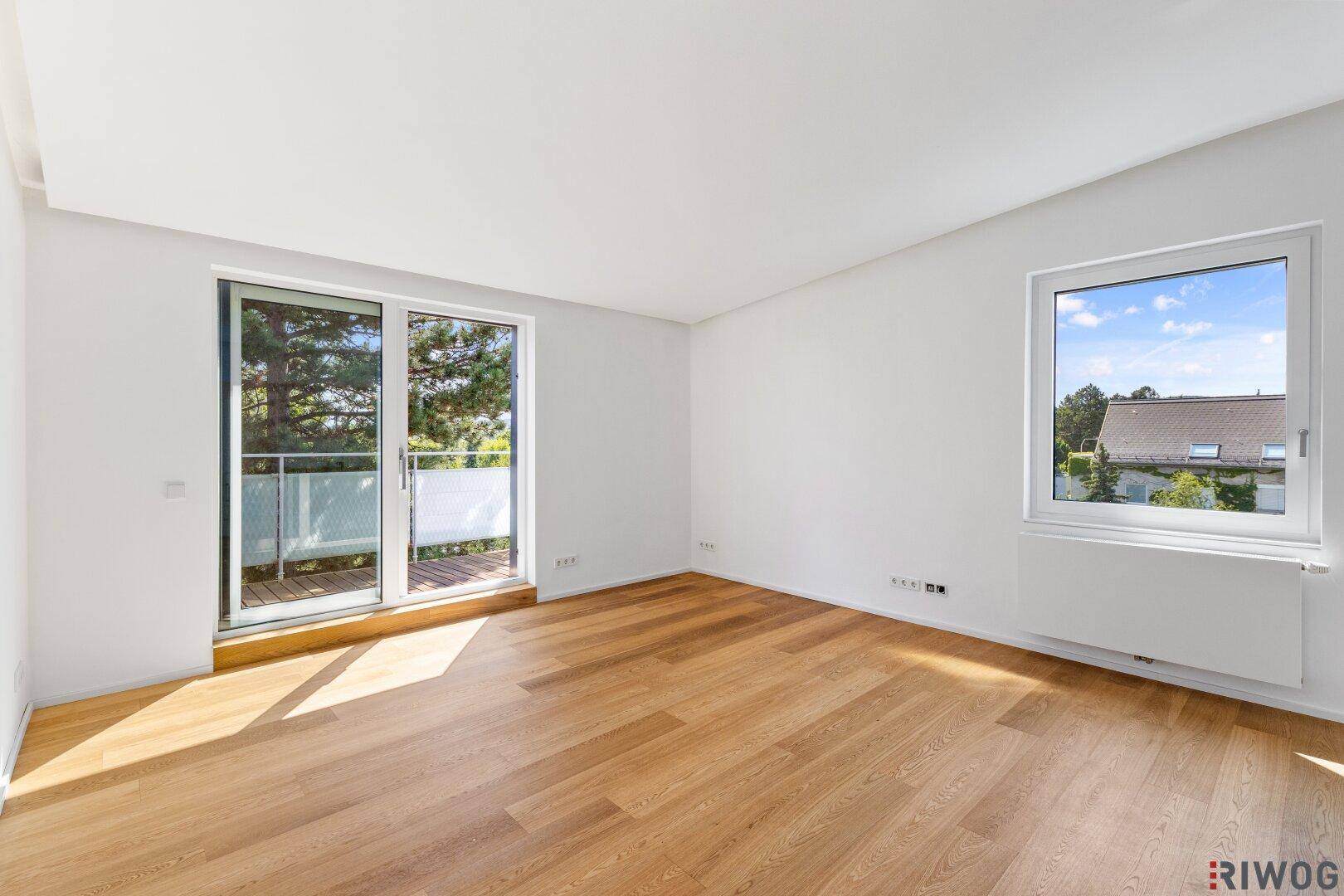 Heller, leerer Raum mit Holzboden, großen Fenstern und Zugang zum Balkon.
