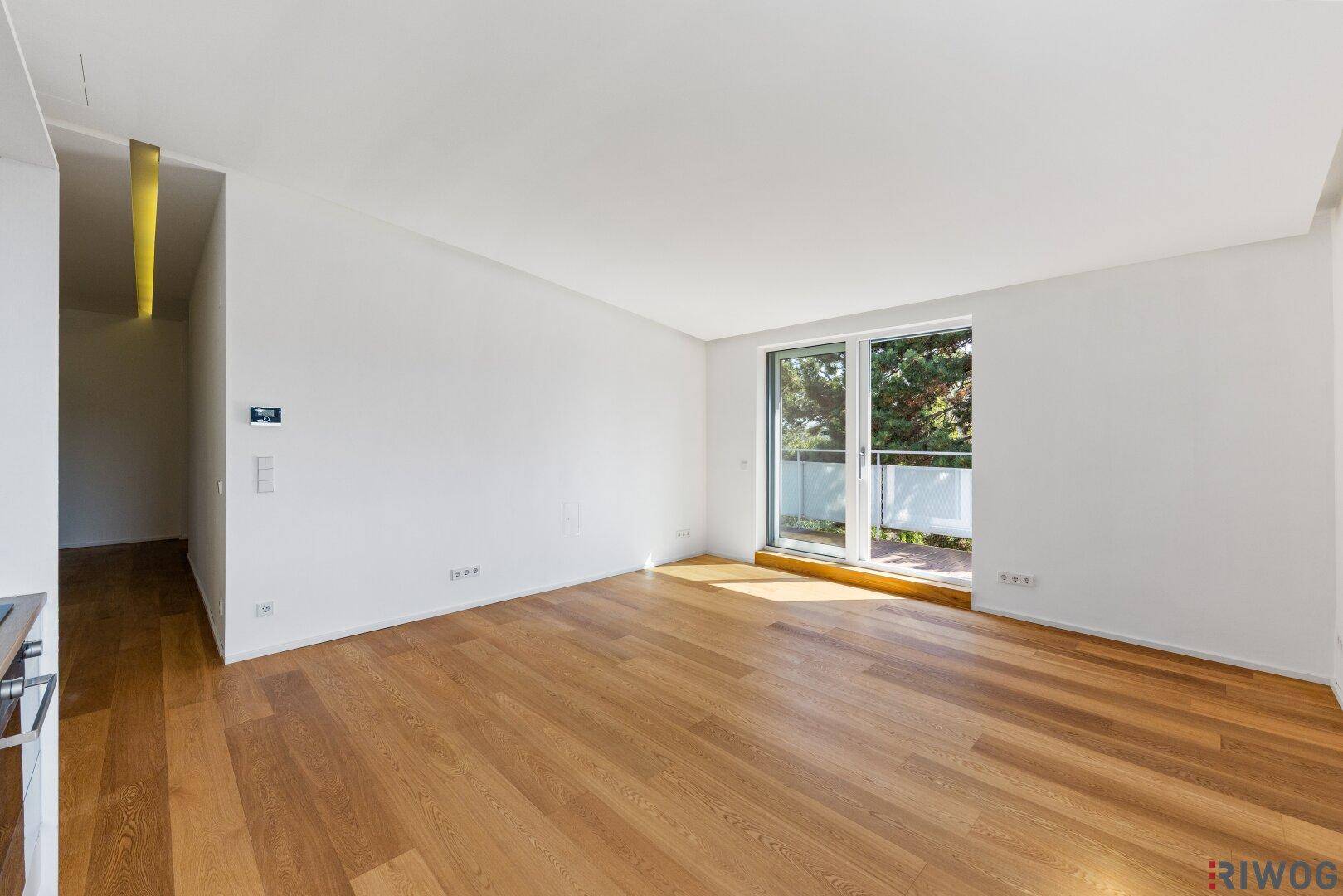 Leerer Wohnbereich mit hellem Holzboden und großem Fenster zum Balkon.